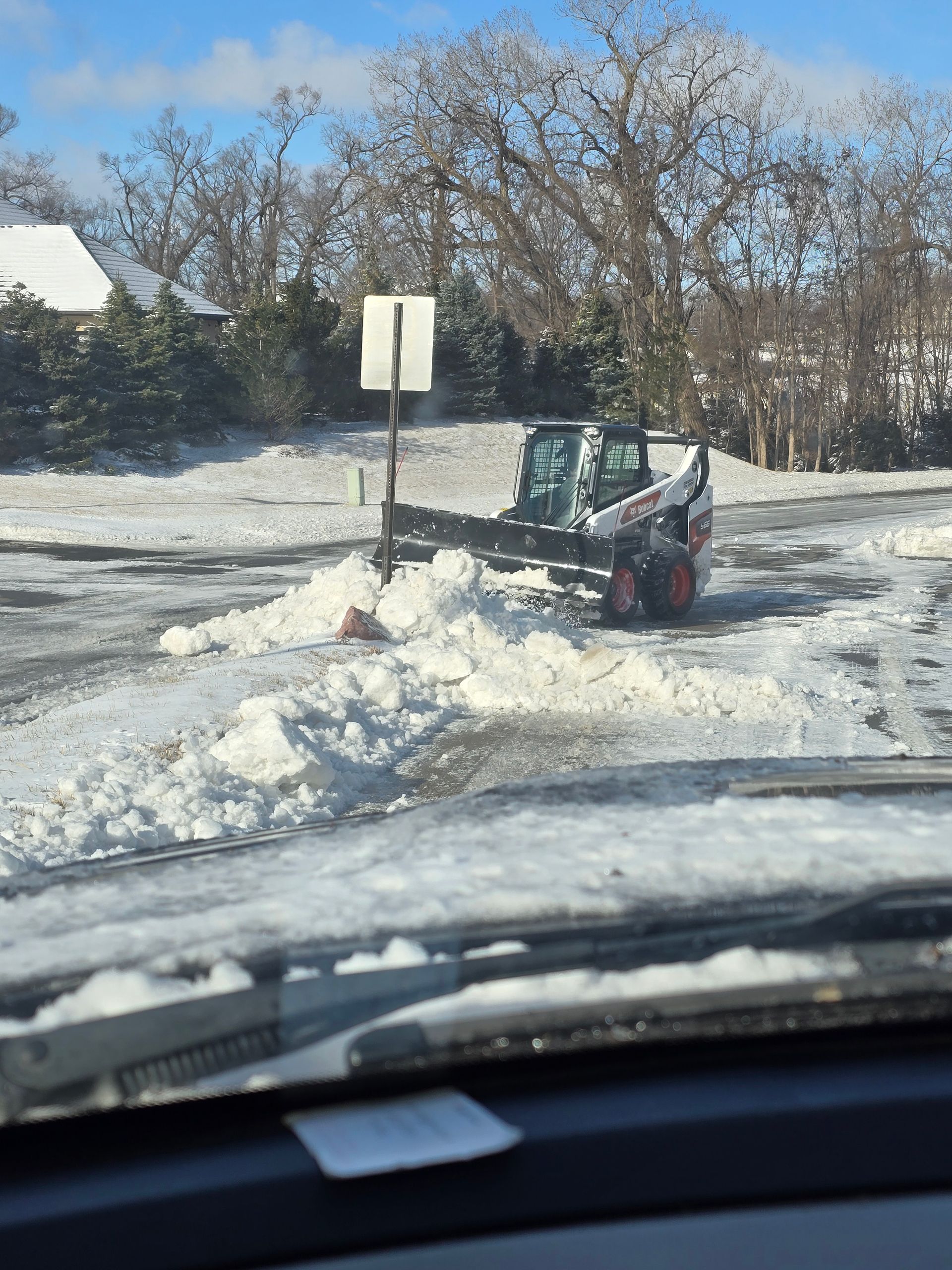 A Bobcat snowplow clearing a snow-covered road on a sunny day.