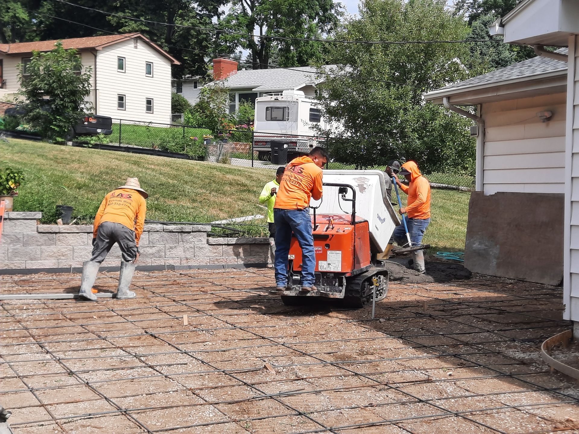 Construction workers pouring concrete for a driveway, using a concrete mixer. Gray wire mesh visible.