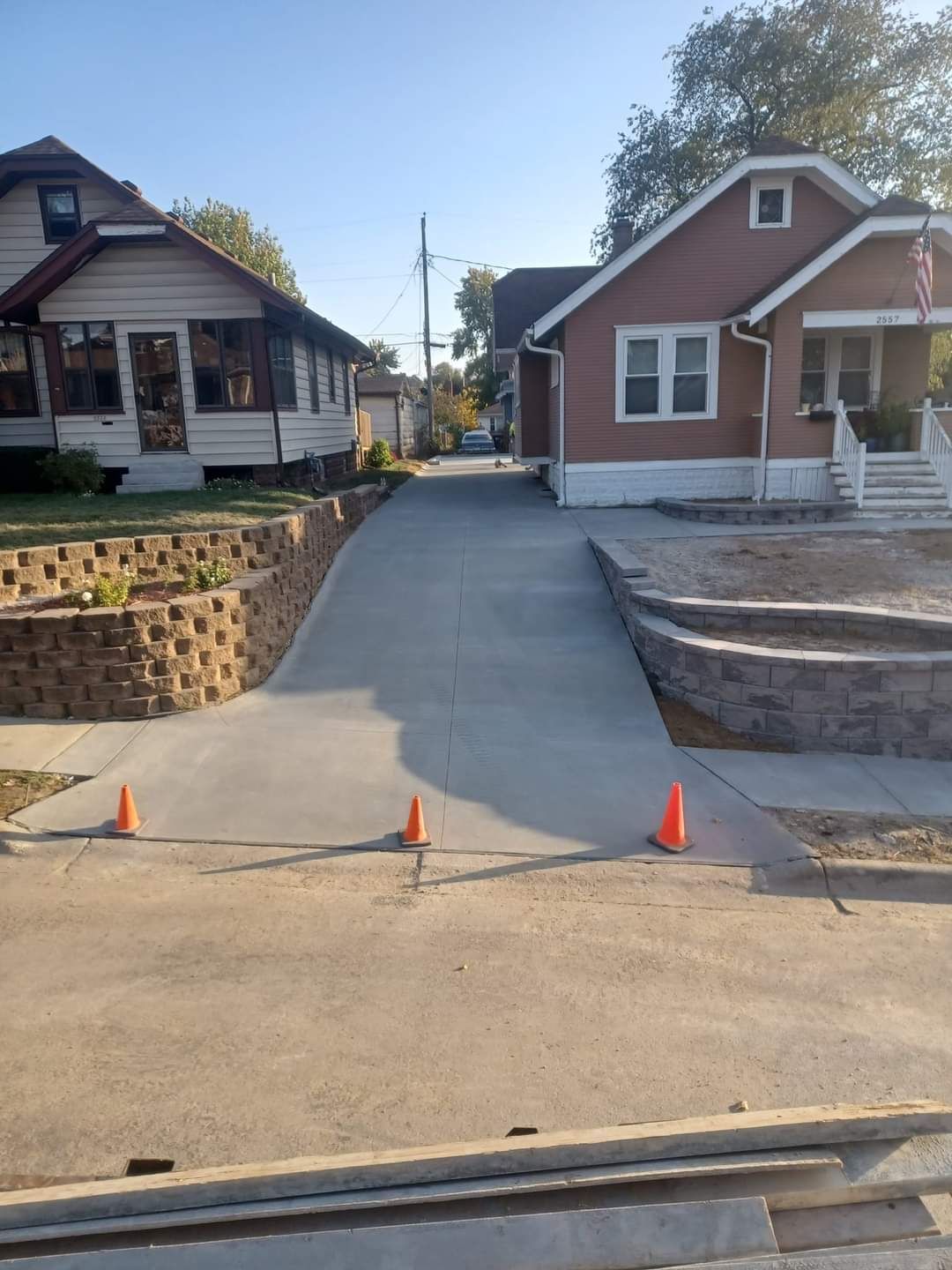 Concrete driveway leading to street, flanked by retaining walls. Two houses are visible on either side.