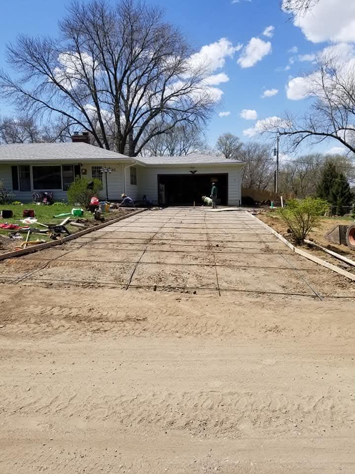 Driveway under construction with exposed rebar, leading to a house and garage on a sunny day.