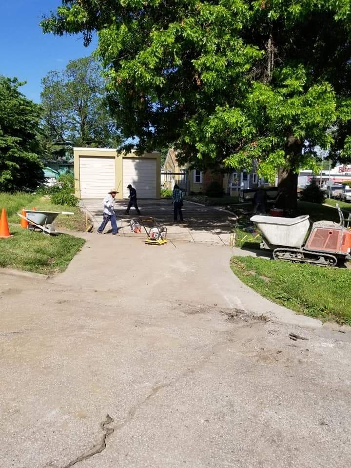 Workers paving a driveway in front of a house and garage on a sunny day.