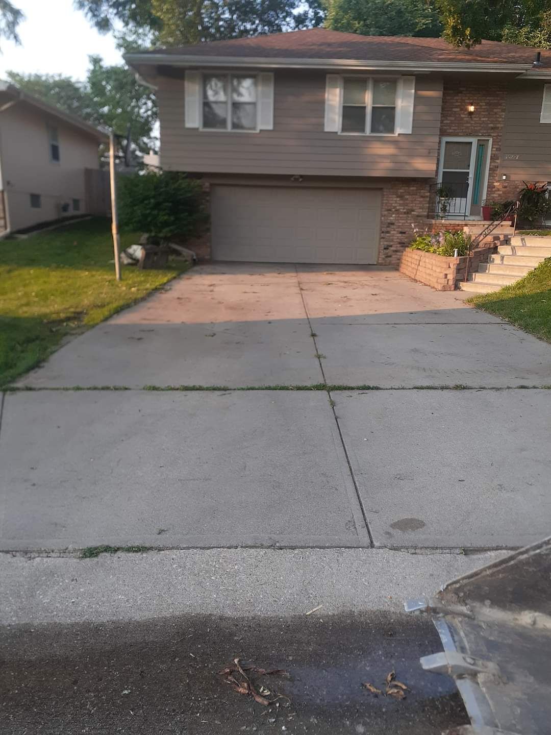 A two-story house with a driveway and garage. Beige siding, stone accents, and a grey garage door.