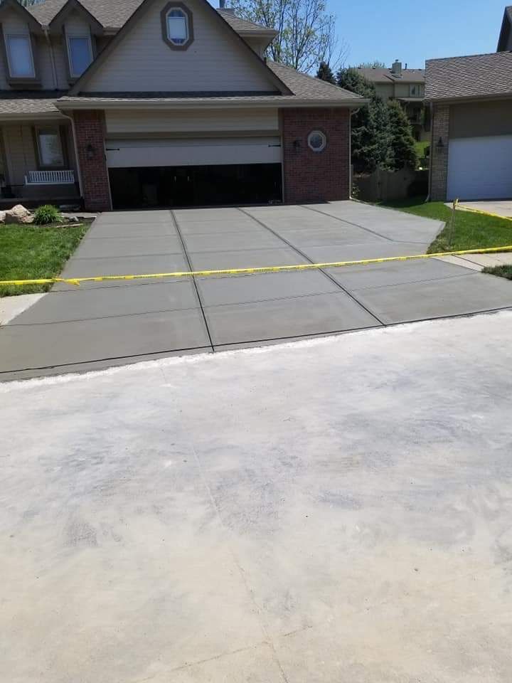 Newly poured concrete driveway in front of a house. Yellow tape divides it into sections.