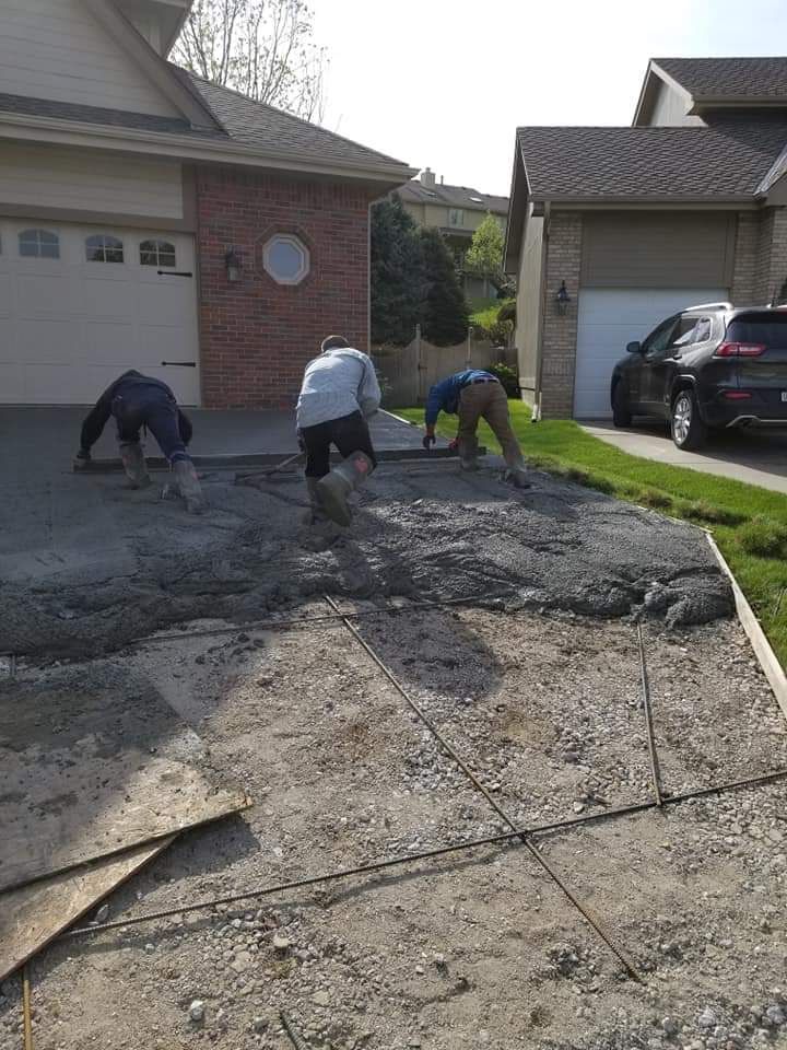 Three people smoothing wet concrete on a driveway in front of a house.