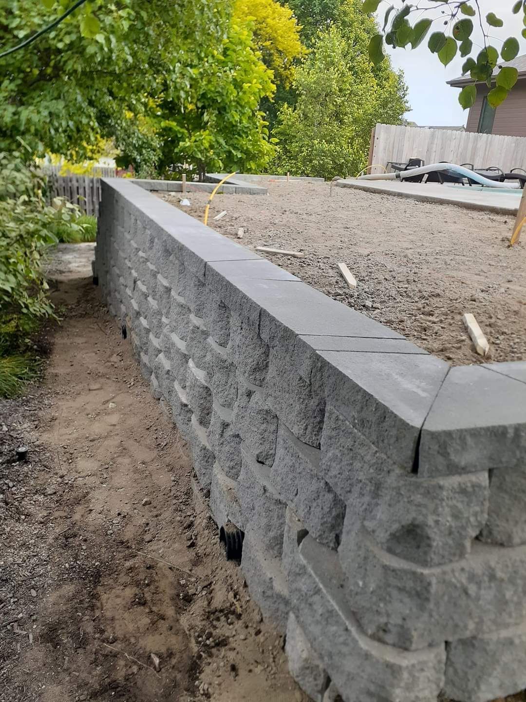 Gray stone retaining wall under construction in a yard.