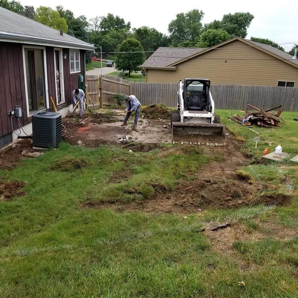 Construction workers using tools and a skid steer in a backyard. Earth is dug up around a house.