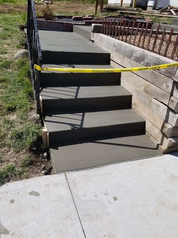 Newly poured concrete steps with yellow caution tape, leading up to a walkway with a retaining wall.