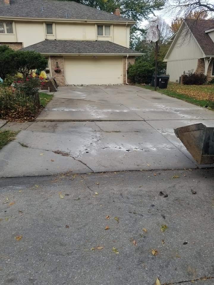 Concrete driveway with cracks leading to a two-car garage. A house is in the background.