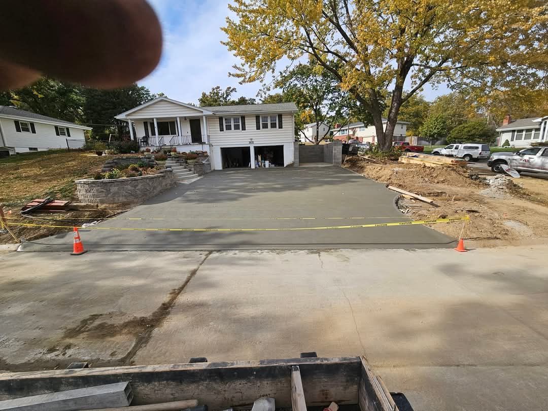 Freshly poured concrete driveway in front of a house, with caution tape and construction materials visible.
