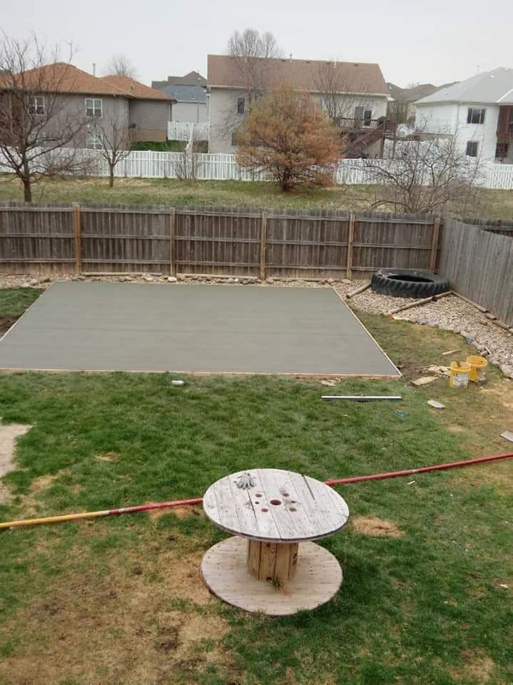New concrete patio in a backyard with a wooden fence and houses.