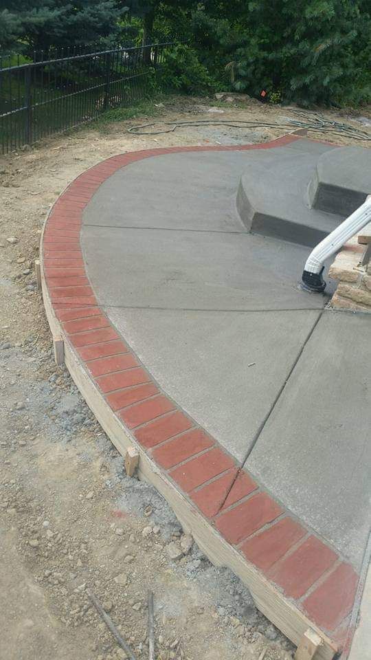 Curved concrete patio with a brick border. Steps and a downspout are visible.
