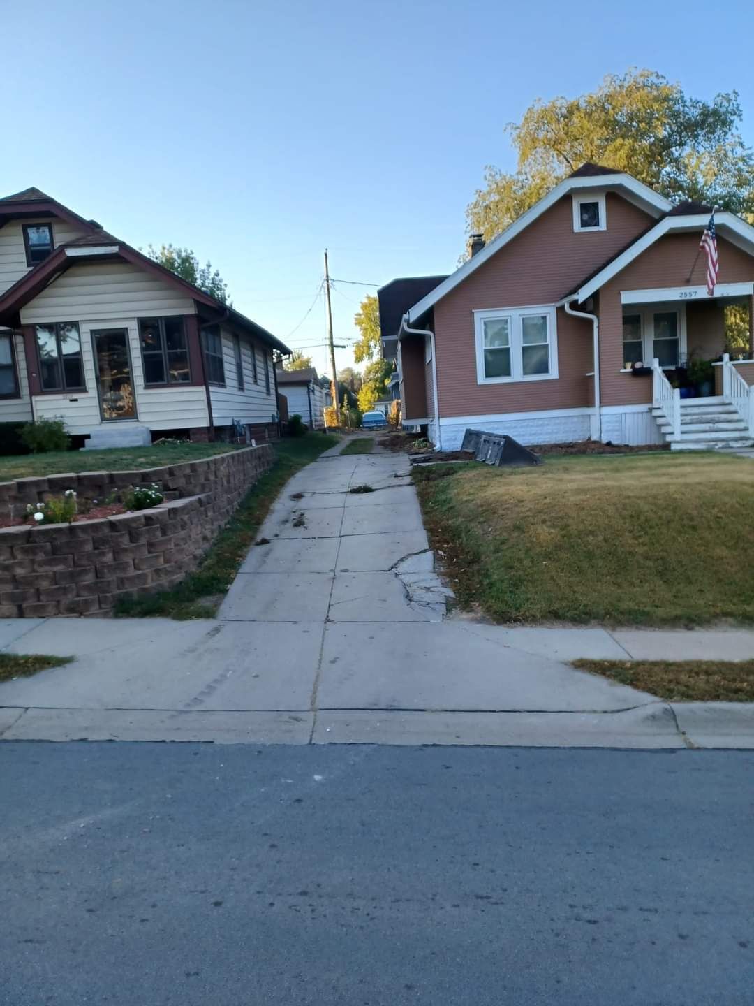 Concrete driveway between two houses; one beige, one pink with white trim. Blue sky.
