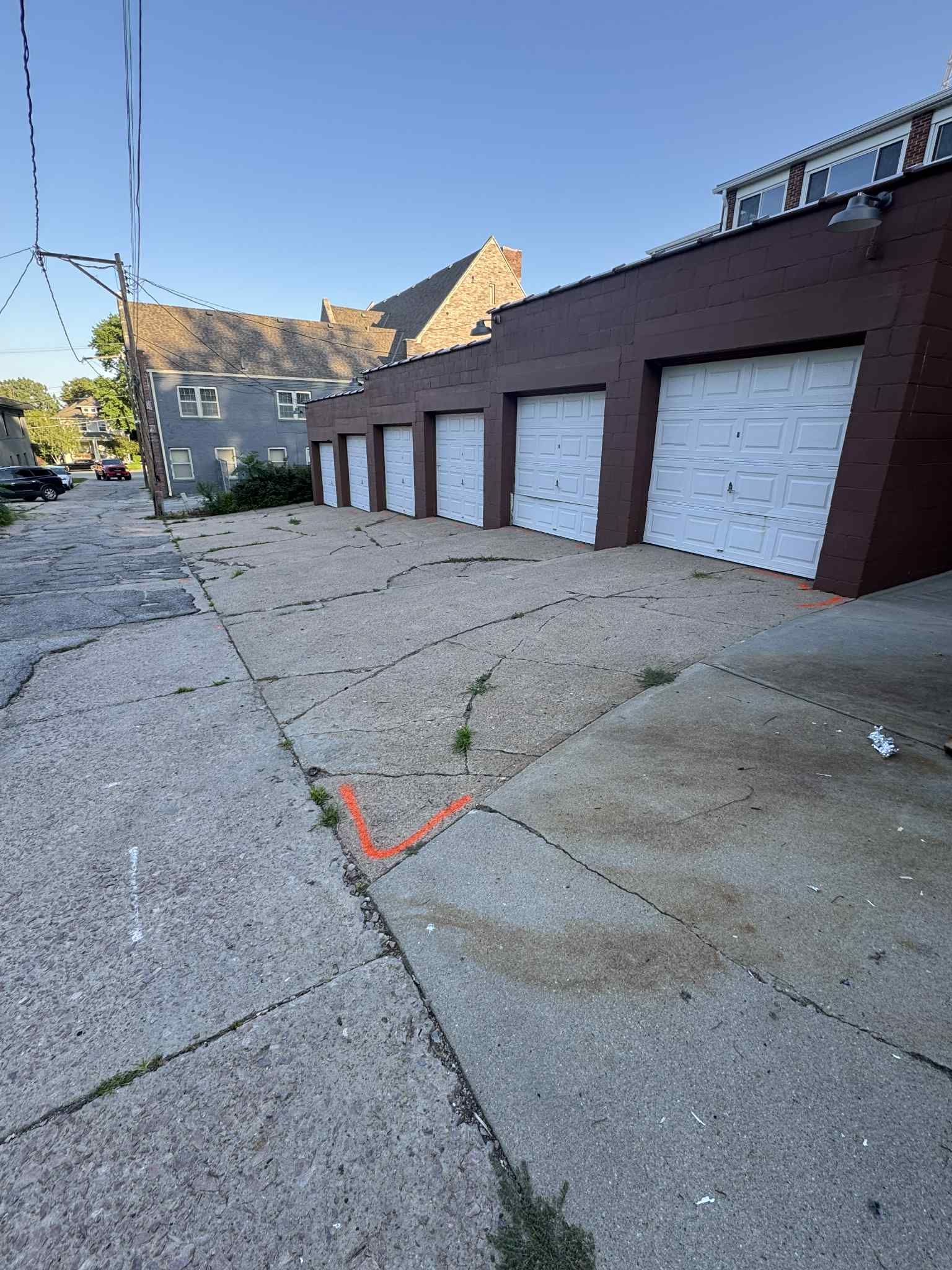 Row of white garage doors on a brick building with a cracked concrete path in front.