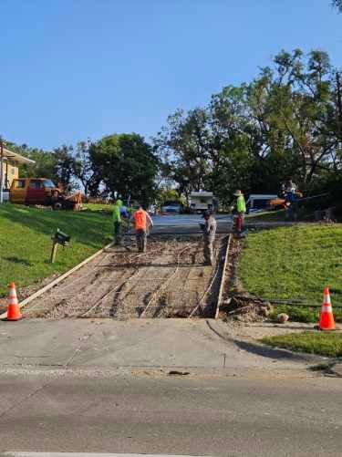 Construction workers pouring concrete on a driveway, with reinforcing bars visible.