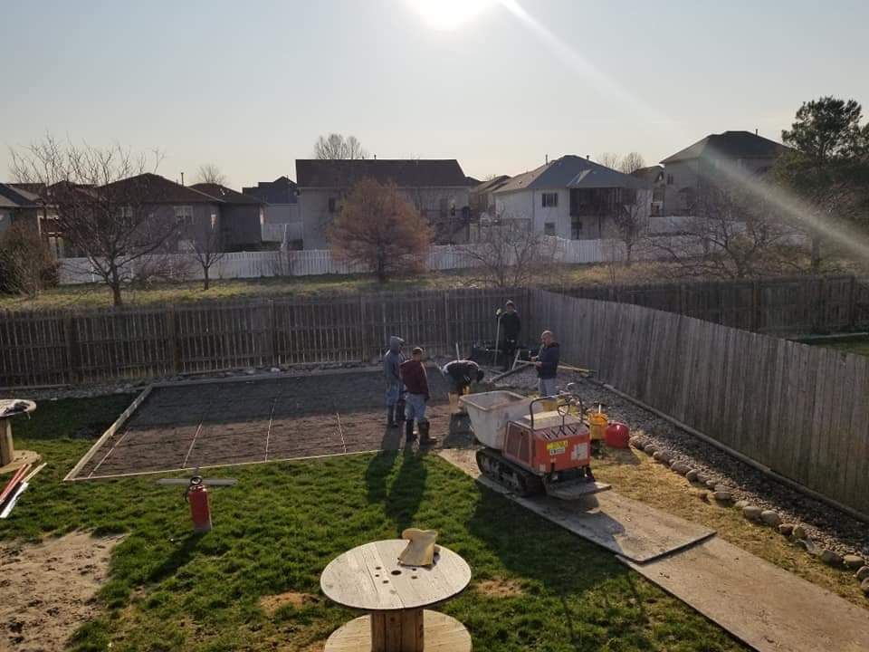 Construction workers in a backyard. A small vehicle and wheelbarrow on a concrete path, working on a square area. Sunny day.