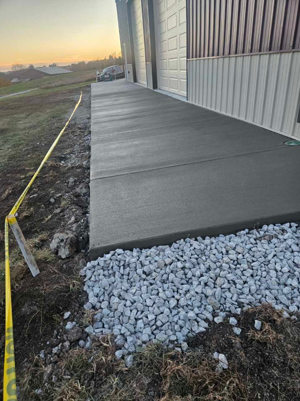 Newly poured concrete sidewalk next to a building, with gravel and caution tape.