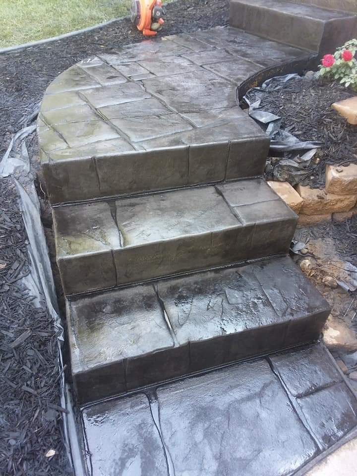 Concrete steps and walkway with a stone pattern, bordered by black mulch and lawn.