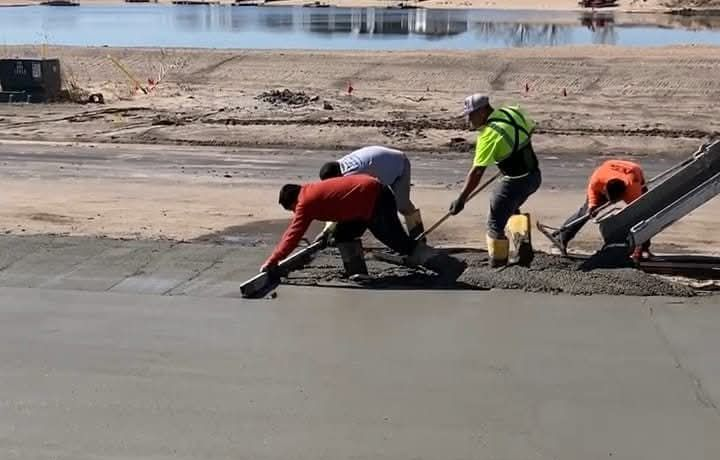 Construction workers smoothing concrete near water.