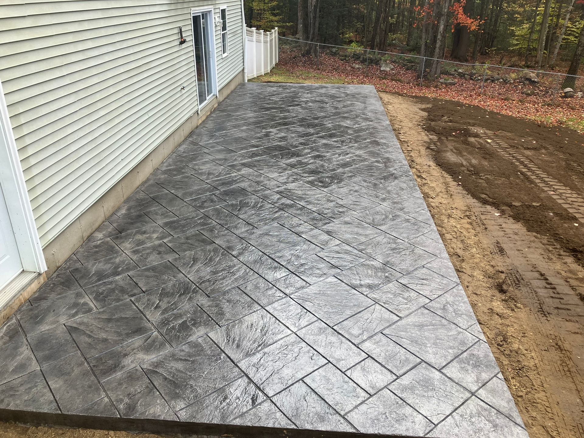 Gray stamped concrete patio next to a house with a door, in a yard.