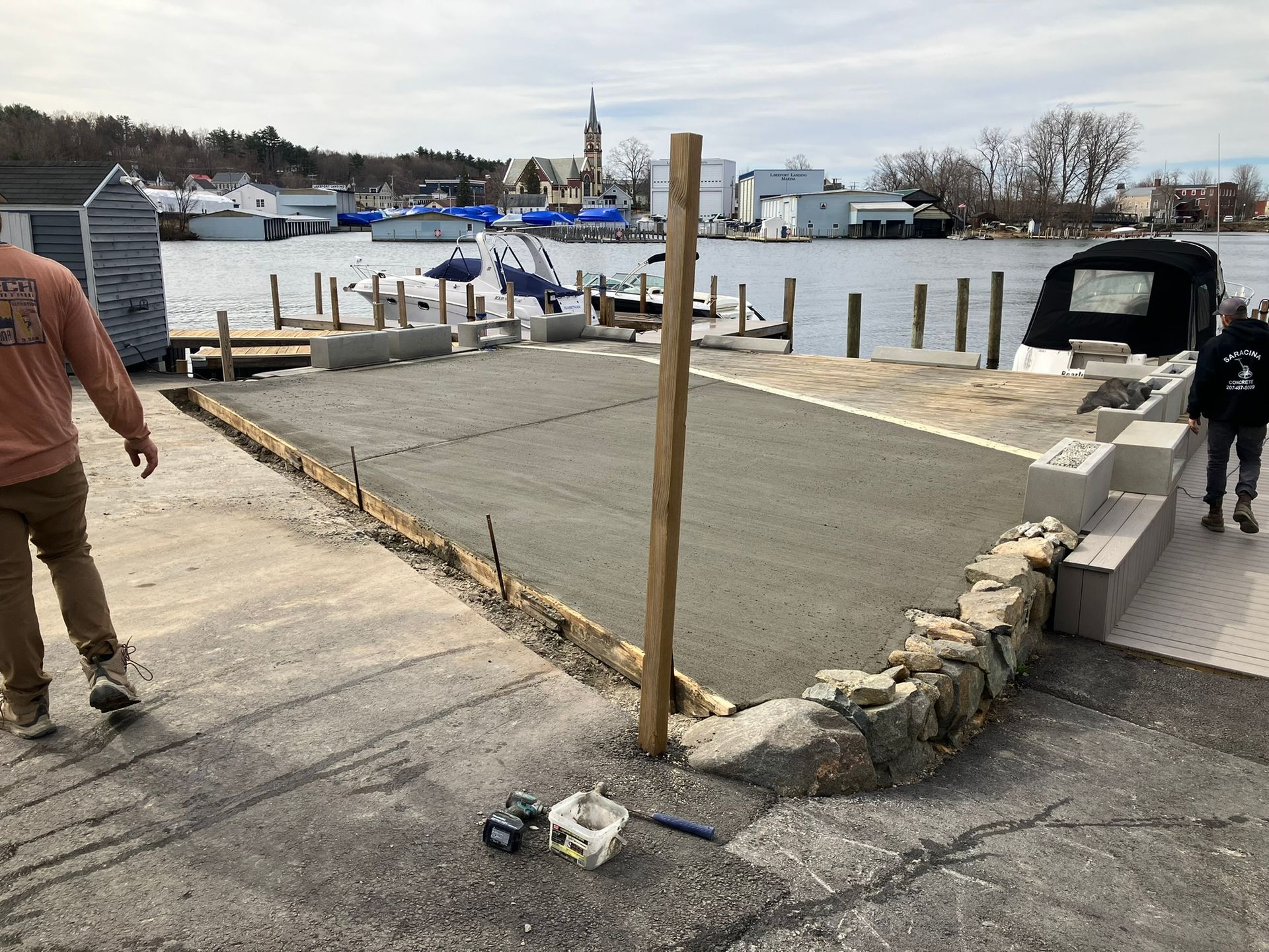 Concrete boat ramp construction with workers near a body of water and boats.
