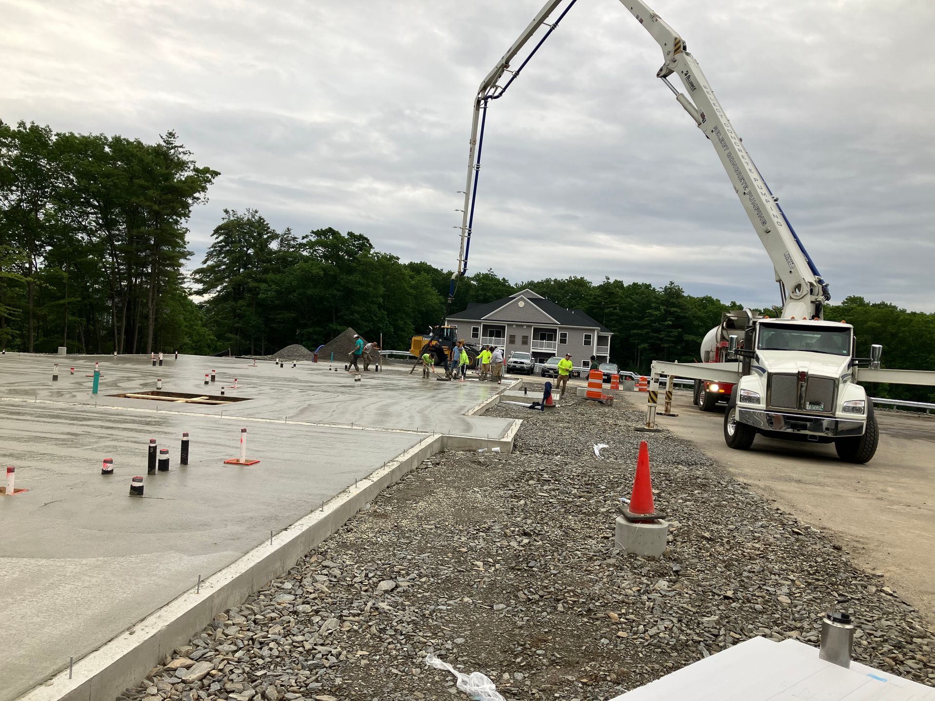 Concrete being poured at a construction site by a pump truck; workers in safety vests; cloudy sky.