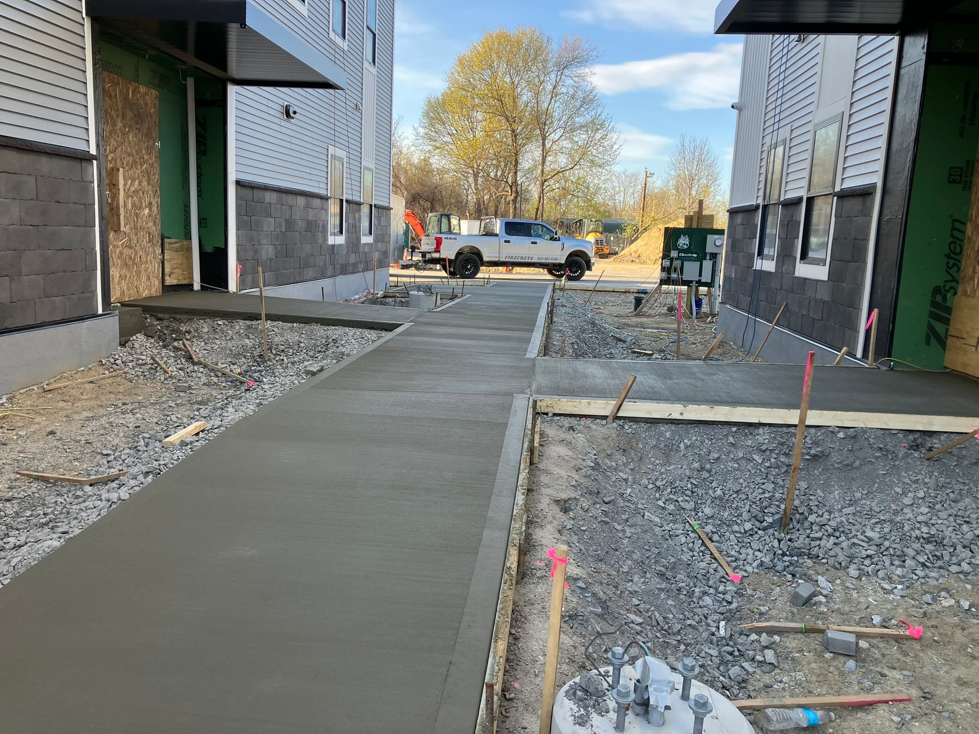 Newly poured concrete walkway between two buildings under construction, with a truck visible in the distance.