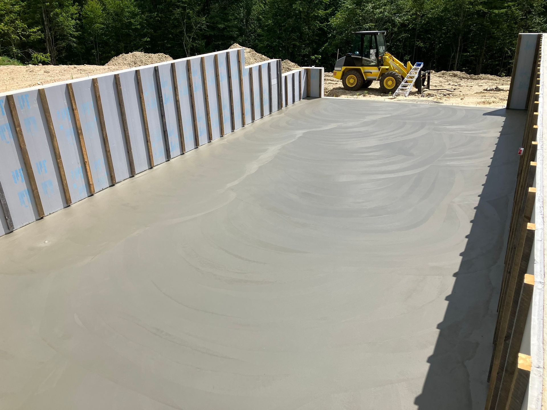 Newly poured concrete floor within insulated concrete form walls, a small loader is in the background.