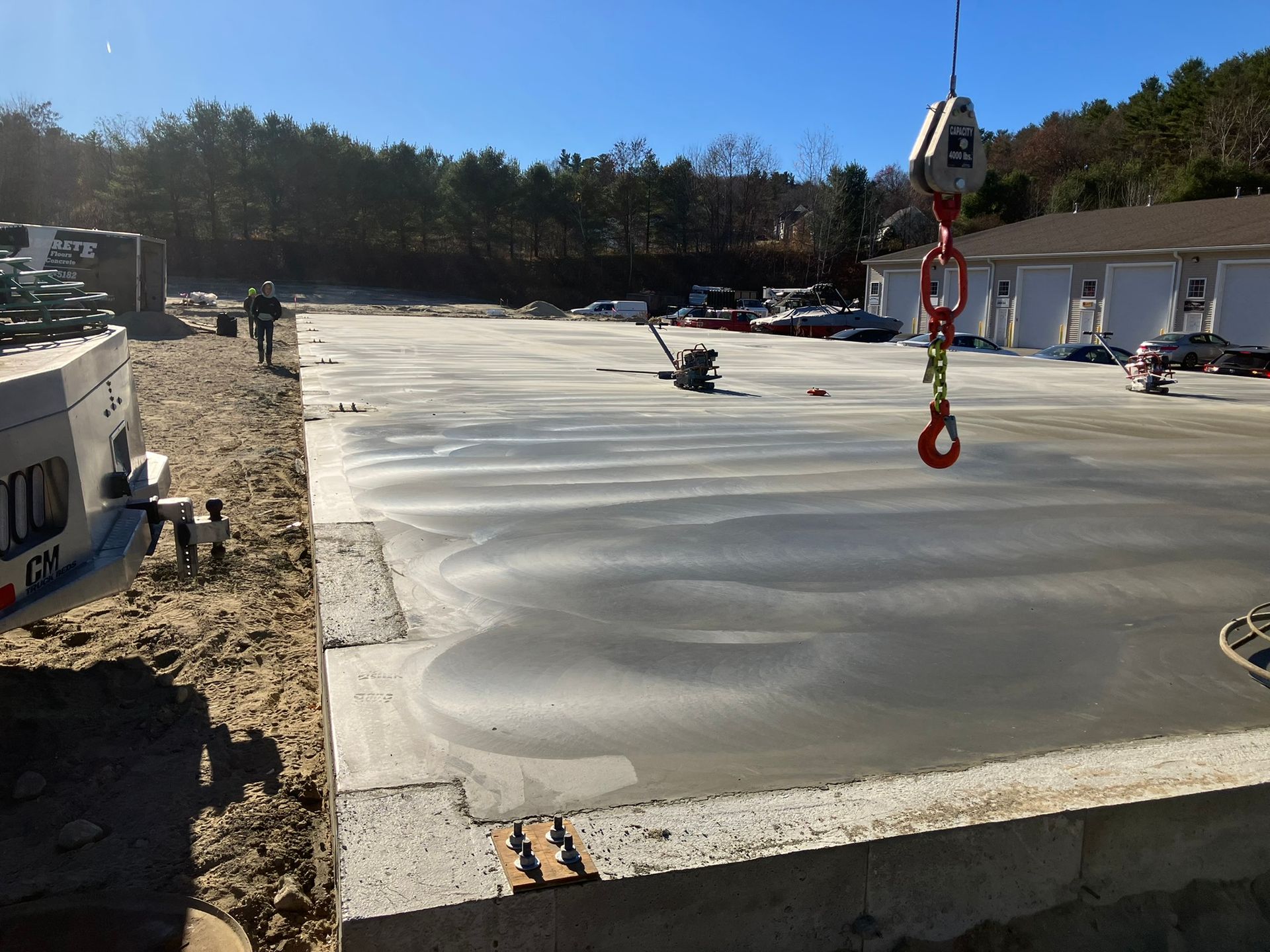 Freshly poured concrete slab being smoothed, with a crane hook and workers nearby.