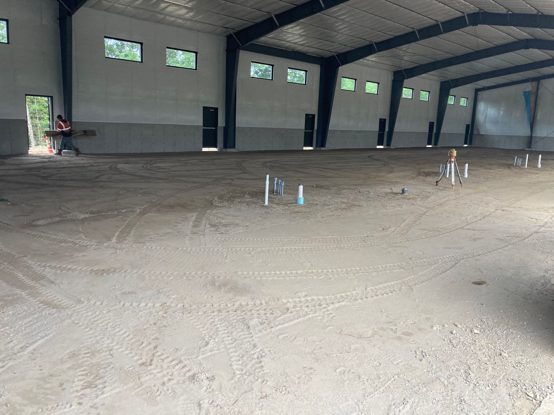 Interior of a large, empty metal building under construction with exposed pipes.