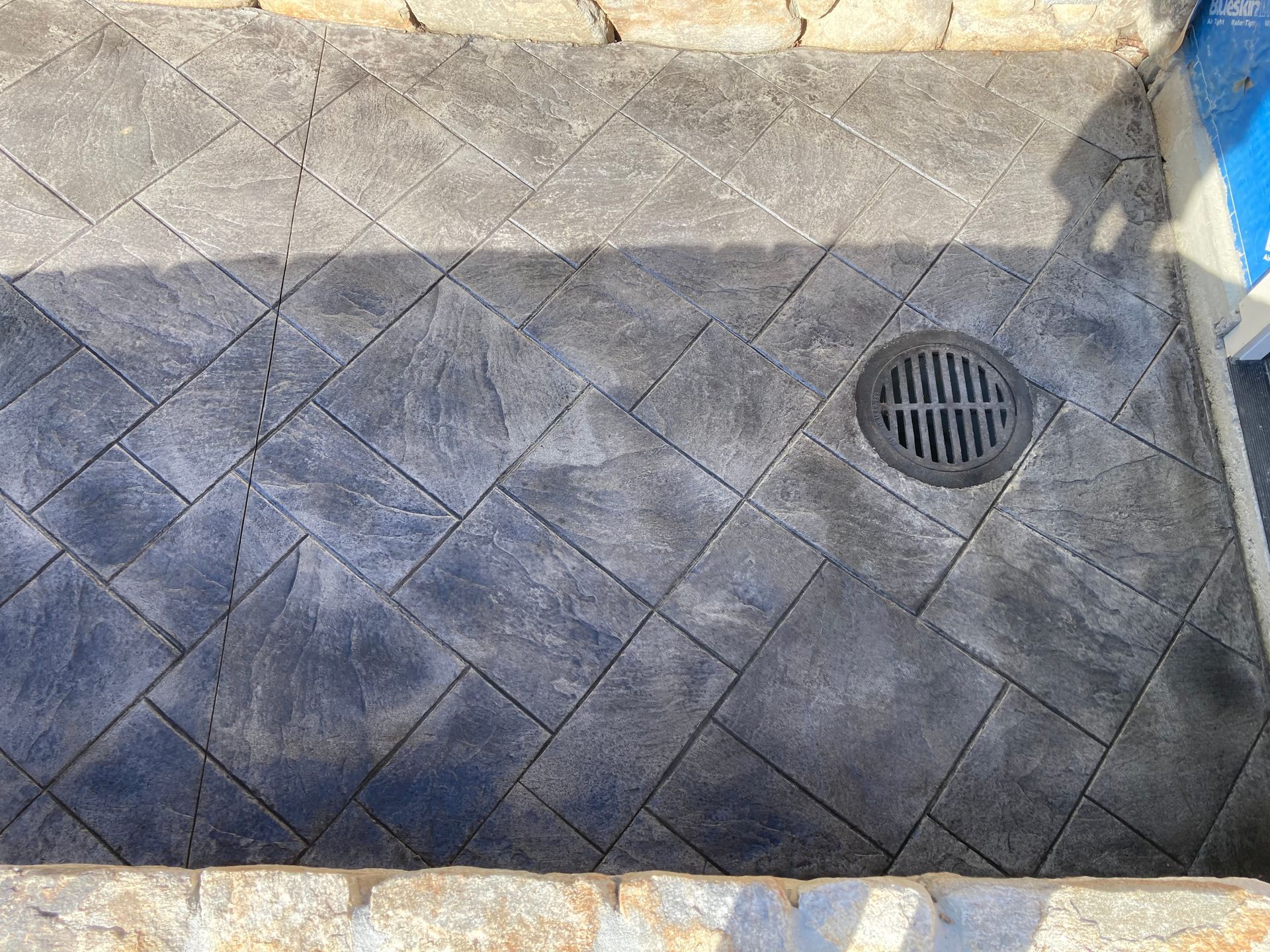 Gray textured concrete patio with diamond pattern and drain.
