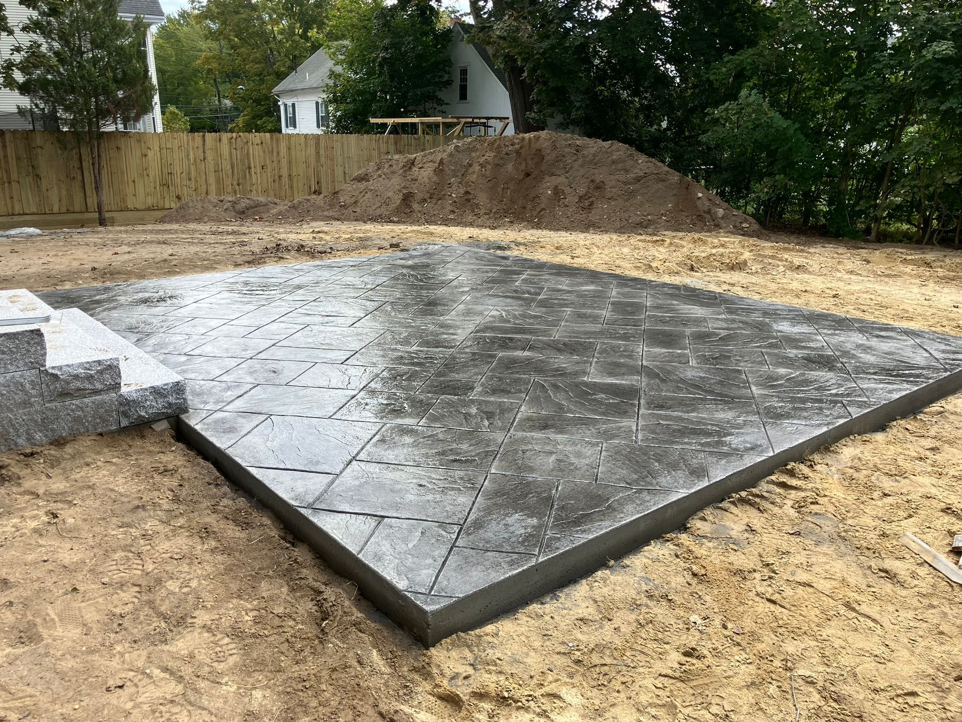 Concrete patio with a patterned surface, surrounded by dirt and a small retaining wall.