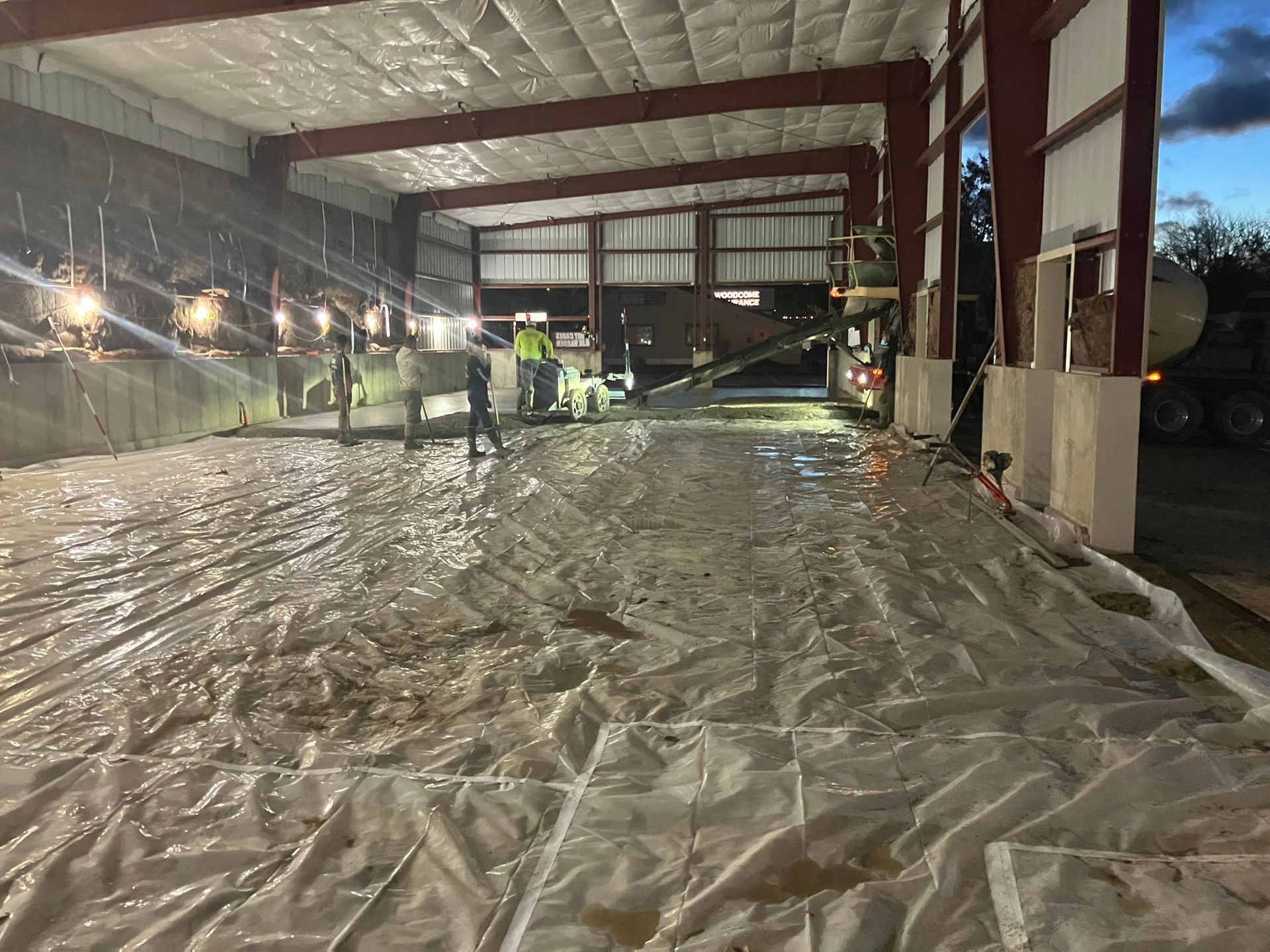 Construction workers pouring concrete inside a building under construction. Tarps cover the ground. Evening setting.