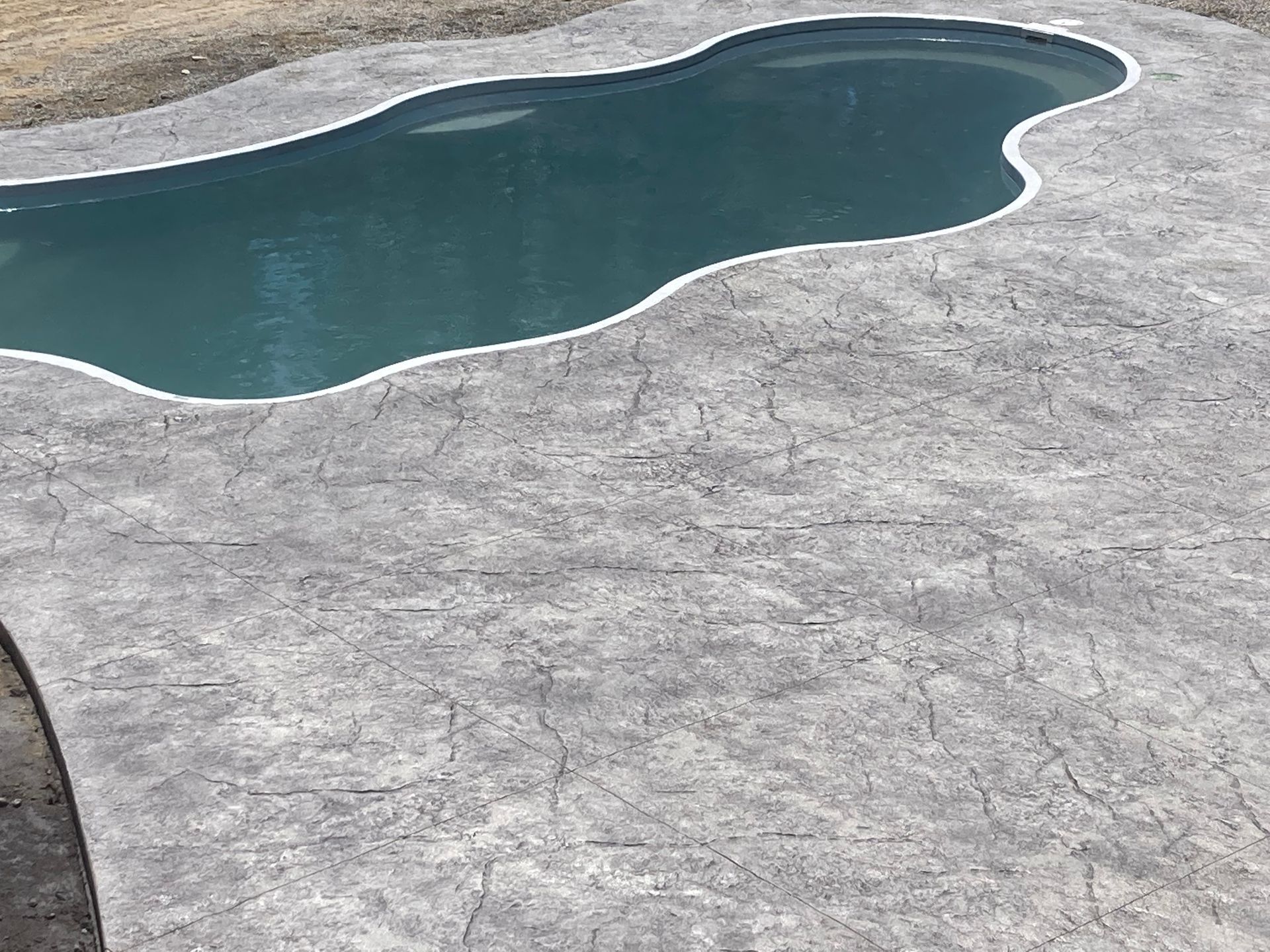 Swimming pool with gray stamped concrete surround.
