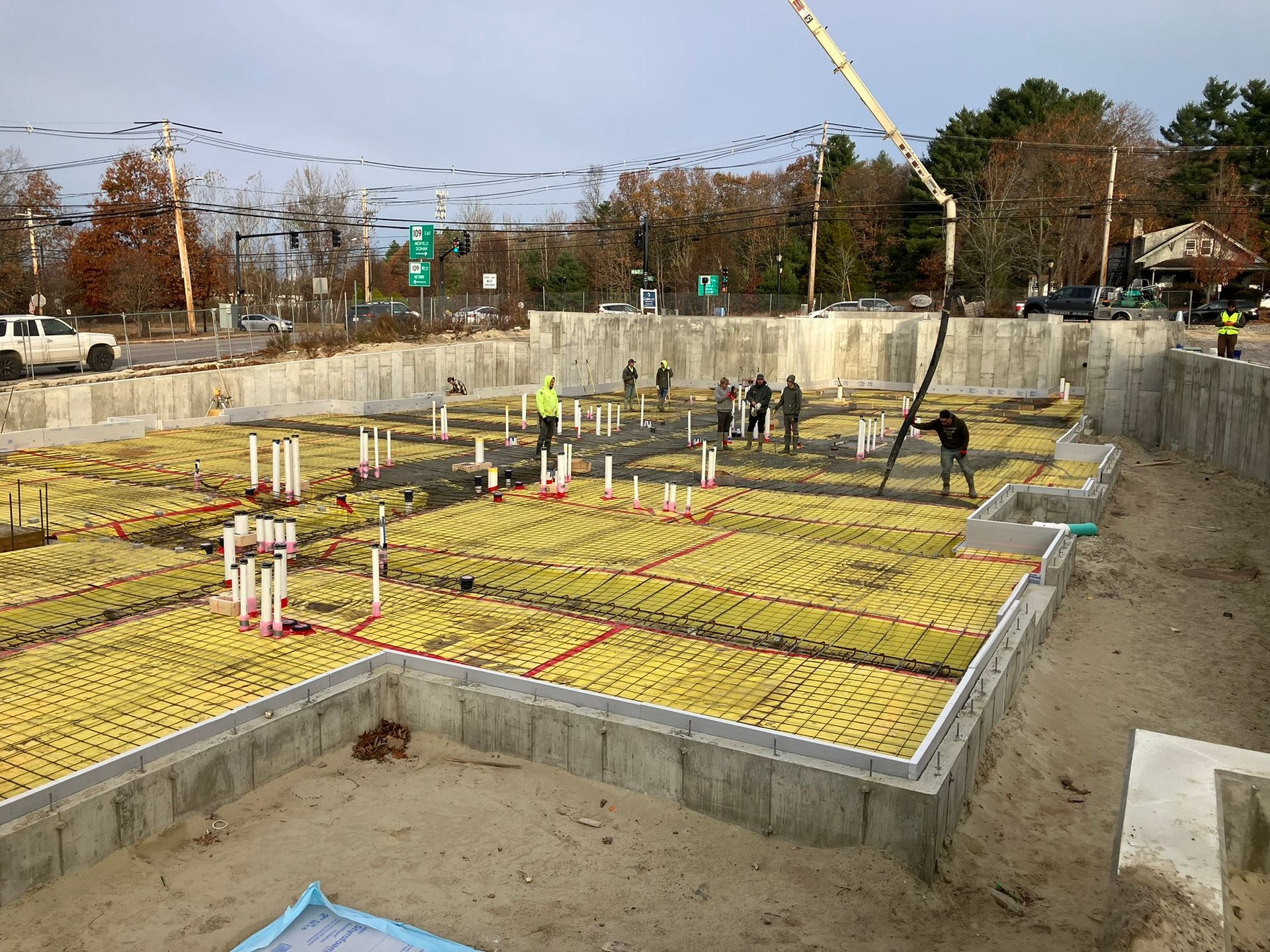 Construction site with concrete foundation and workers; a pump truck pours concrete.