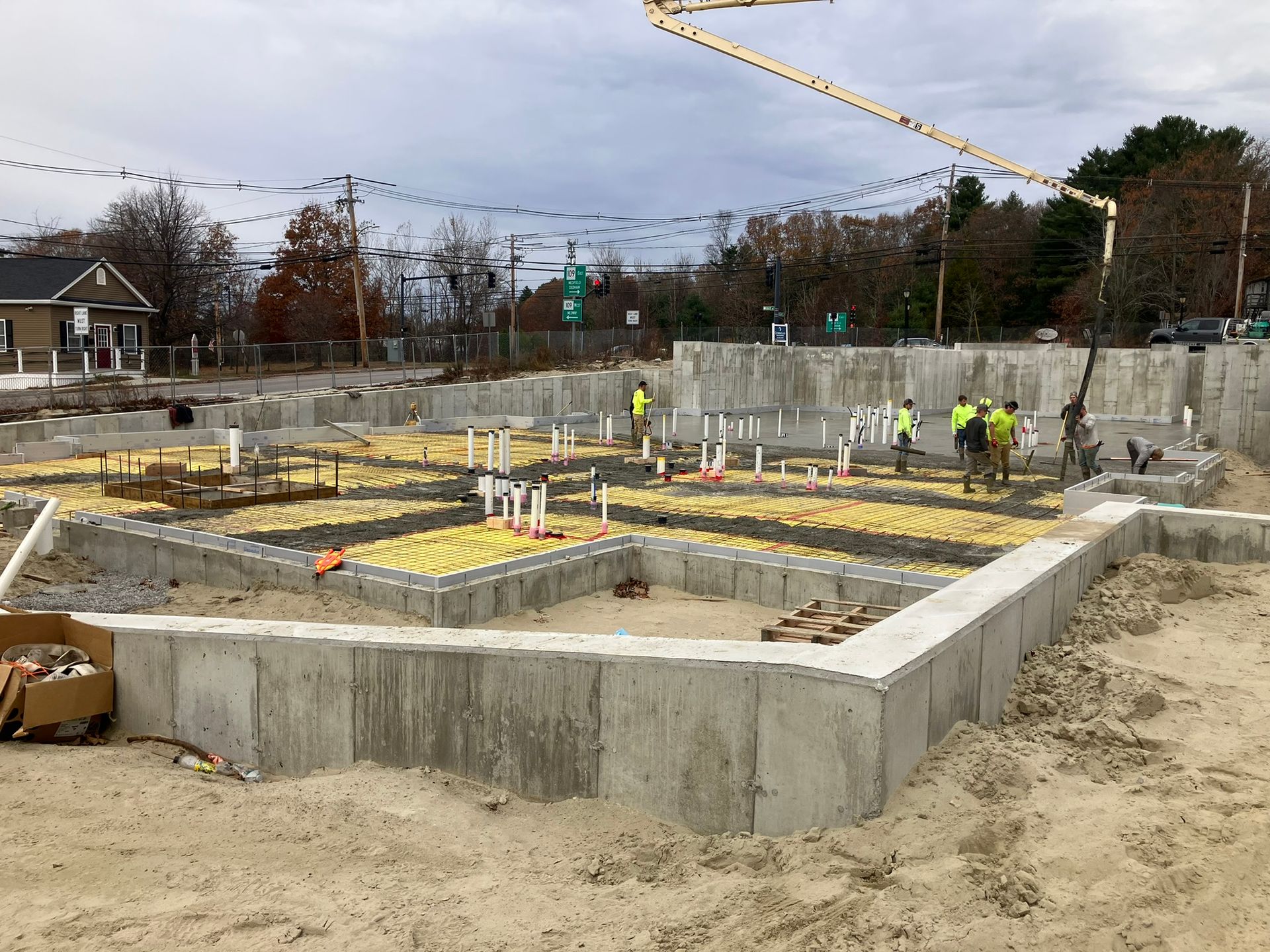 Construction site: Concrete foundation walls with plumbing, workers, and a concrete pump.
