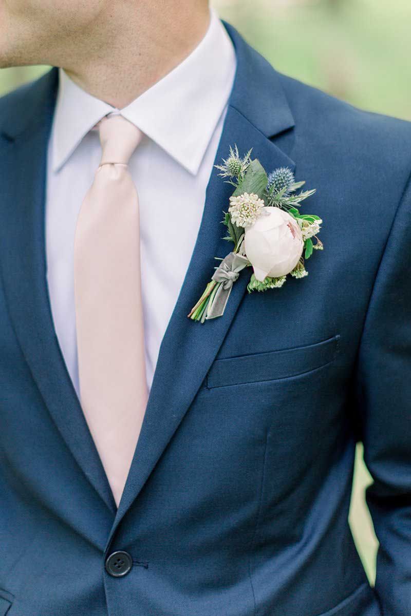The groom is wearing a blue suit and a pink tie.