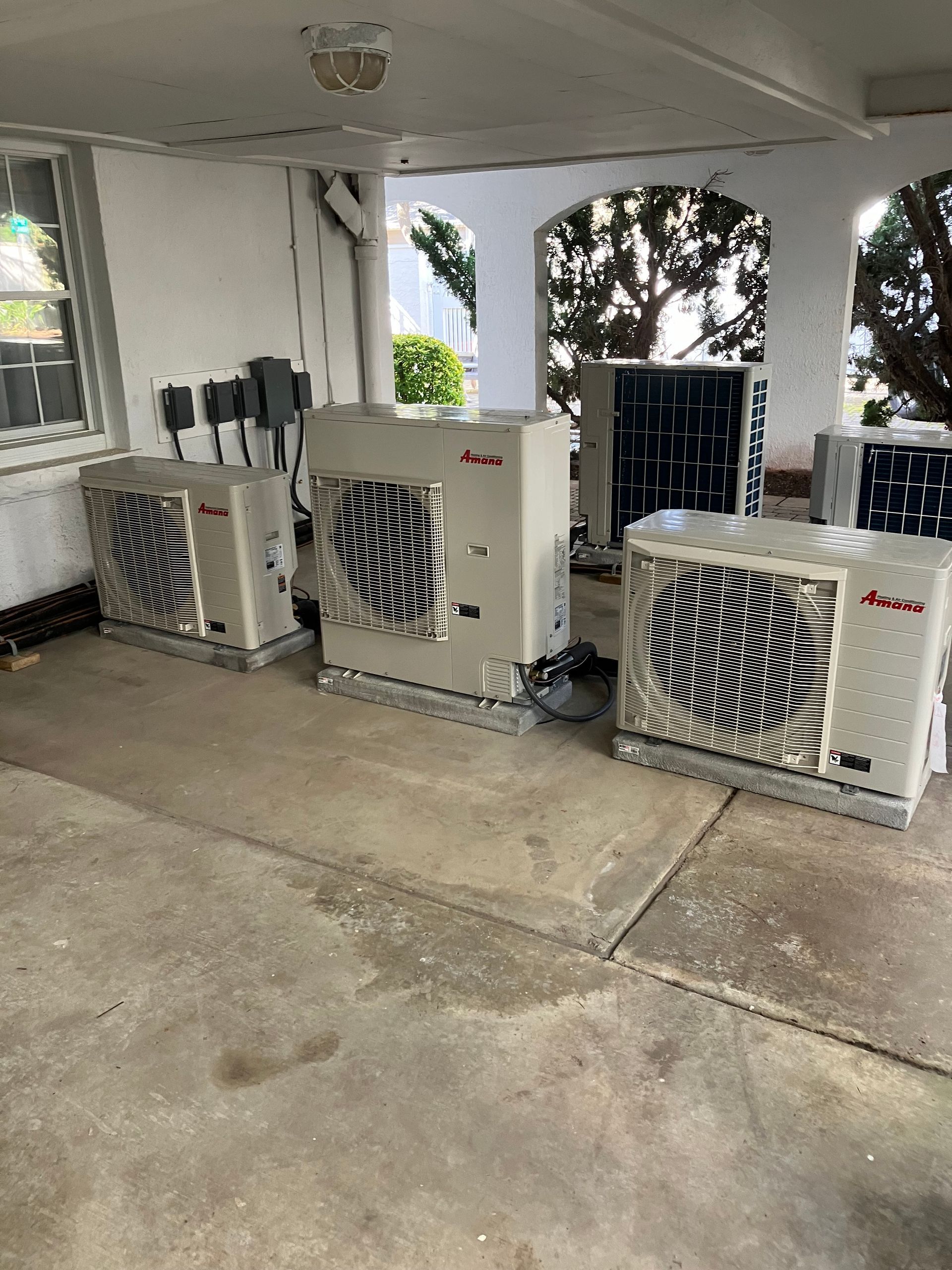 A row of air conditioners are sitting under a covered porch.