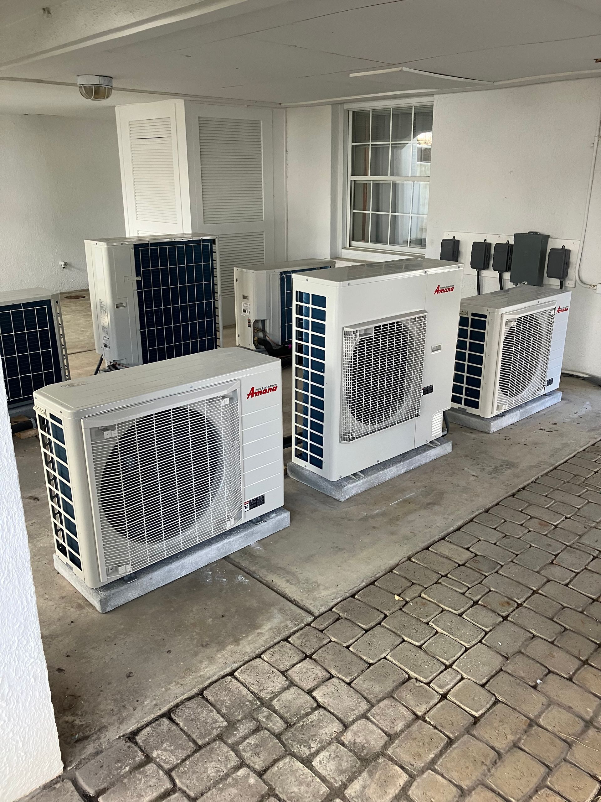 Three air conditioners are sitting on a brick floor in a room.