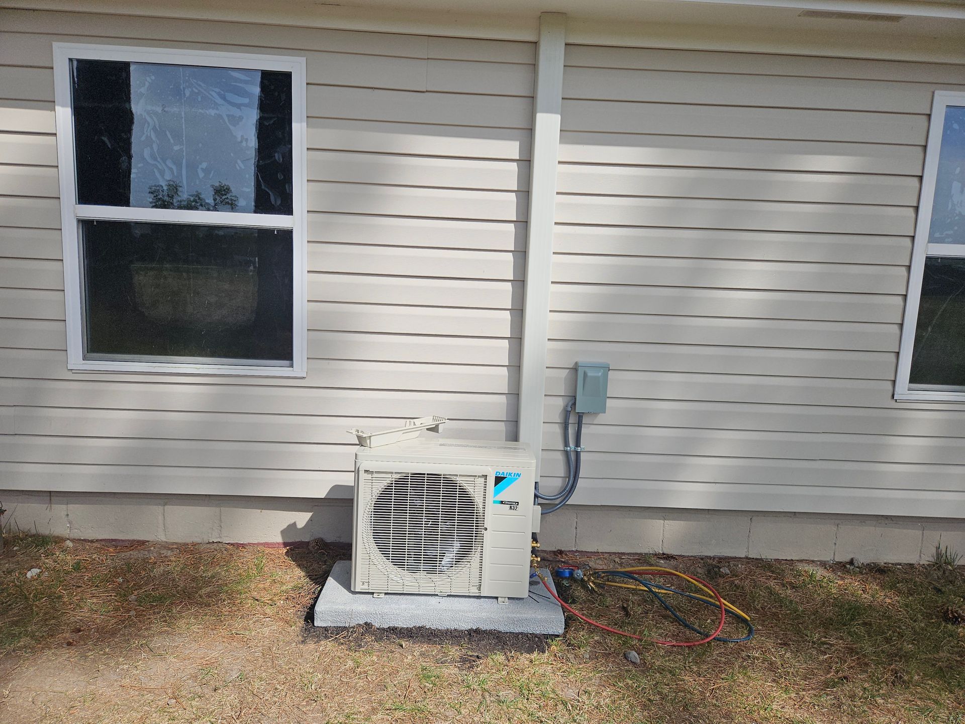 One white air conditioning machine outside a white housed next to window.