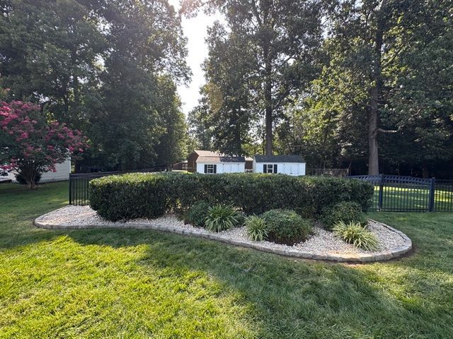 Landscaped yard with a curved rock bed, trimmed shrubs, and tall trees behind a black fence.