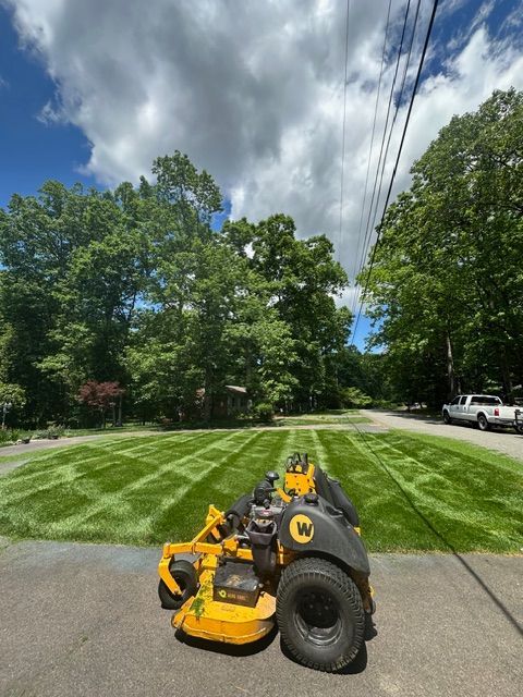 Yellow lawn mower on freshly striped grass beside a road under a cloudy sky