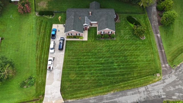 Aerial view of a suburban house with a large green lawn and several cars in the driveway.