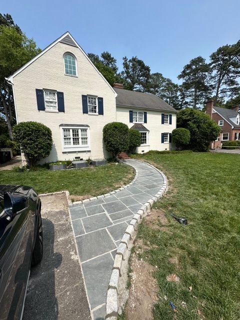 White two-story house with blue shutters and stone walkway in a suburban yard