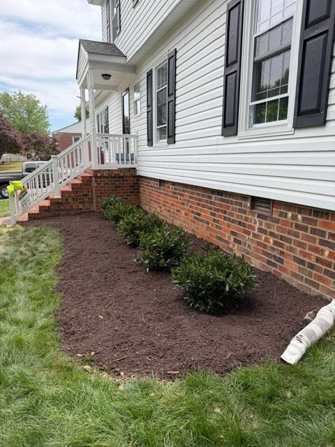 White house exterior with brick foundation, newly mulched flower bed, and black shutters beside a lawn