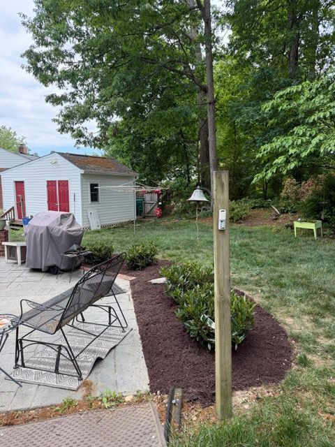 Backyard patio with lounge chairs, a young tree, red mulch bed, and a small white shed in the background