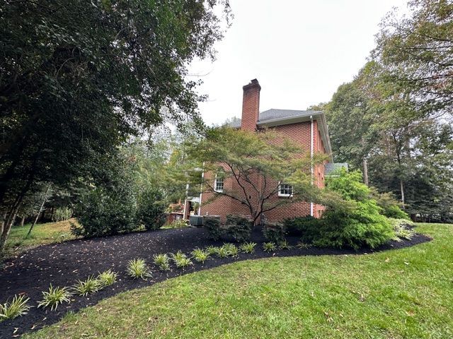 Red brick house with chimney, surrounded by trees and a landscaped front yard with dark mulch.