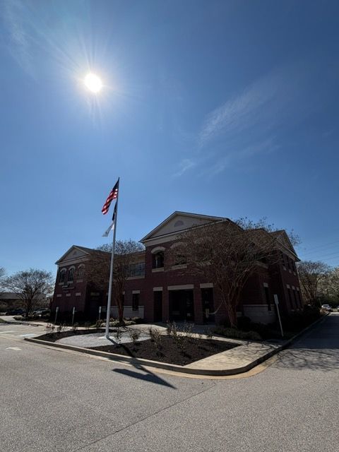 Brick civic building with a U.S. flag on a sunny street corner under a clear blue sky