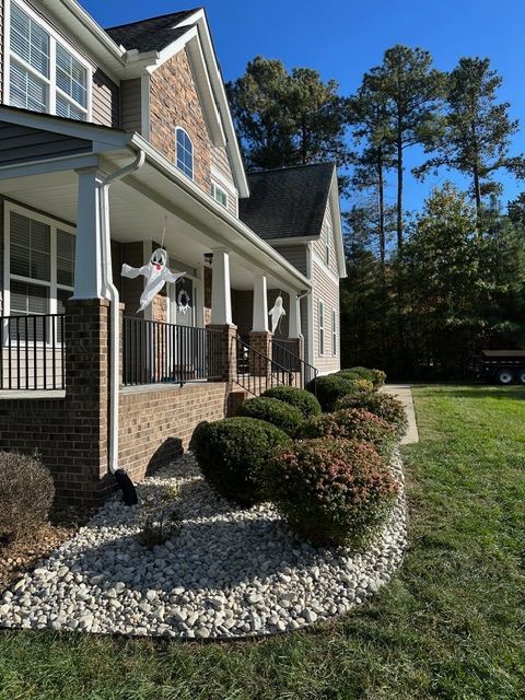 Brick house front porch with white columns, landscaped shrubs, and two people standing outside.