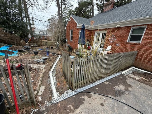 Backyard with patio, wooden fence, red brick house, and narrow snowy path by garden beds
