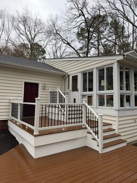 Wooden deck with white railing and steps beside a beige house with large windows and a red door.
